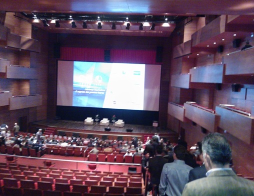 Vista do palco com o painel do Fórum com os participantes tomando seus lugares
